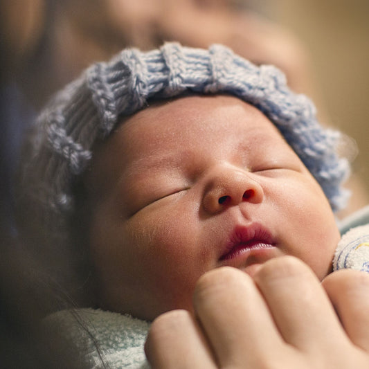Nouveau-né endormi avec bonnet tricoté bleu, bébé emmailloté chez maternité.