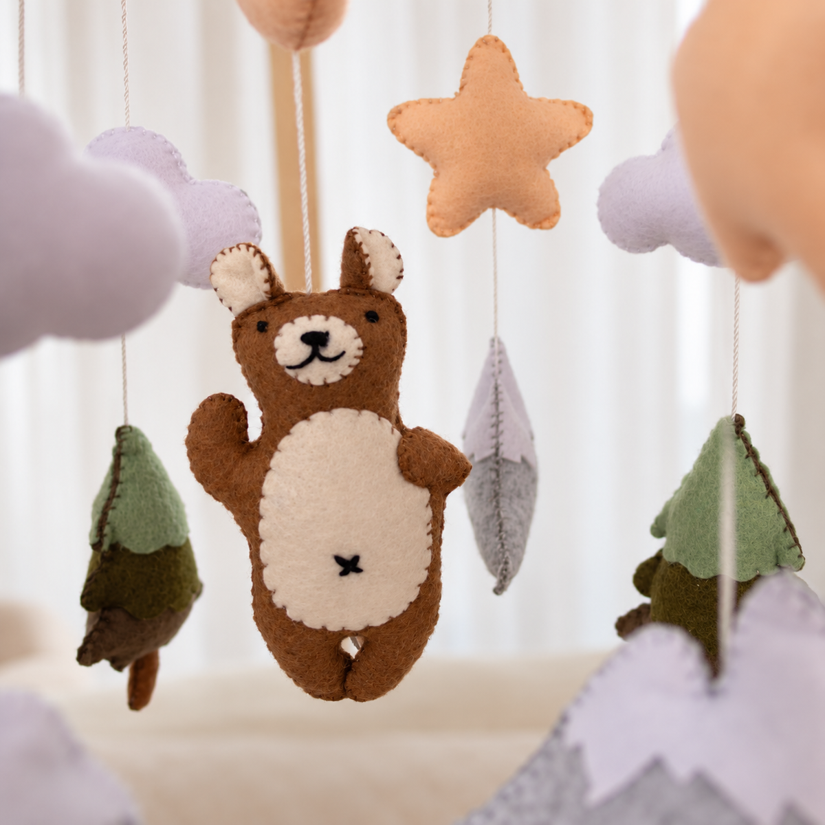 Mobile bébé Ours brun suspendu au-dessus d’un lit dans une chambre aux tons naturels