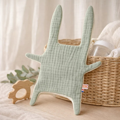 Doudou_lapin_vert_sauge_en_coton_bio_pos_sur_surface_en_bois_clair_avec_panier_en_osier