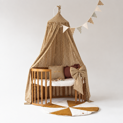 Ciel de lit bébé rayures olive au-dessus d’un berceau ovale en bois